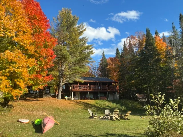 The Waterfront Cottage surrounded by colourful autumn trees with a lawn, fire pit and watercraft